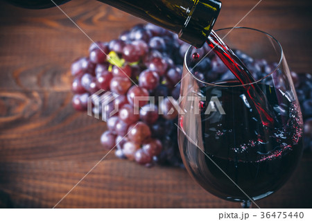 Pouring red wine into the glass with a bunch red  36475440