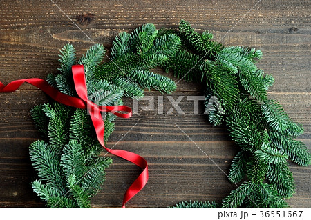 モミと赤いリボンのクリスマスリース 黒木材背景の写真素材