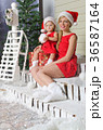 Mom and daughter in Santa's suits are sitting under snow 36587164