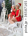 happy mom and daughter in Santa's suits are sitting under snow 36587165