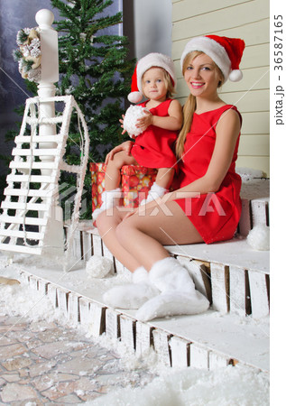 happy mom and daughter in Santa's suits are sitting under snow happy mom and daughter in Santa's suits are sitting under snow 36587165