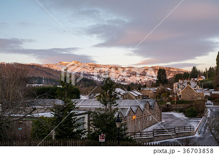 スコットランド郊外の雪の中の小さな町と遠くに見える夕焼けで赤くなる雪山 36703858