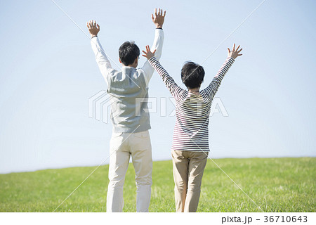 草原で両手を挙げるシニア夫婦の後姿の写真素材