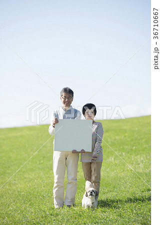 草原でメッセージボードを持つシニア夫婦と犬 36710667
