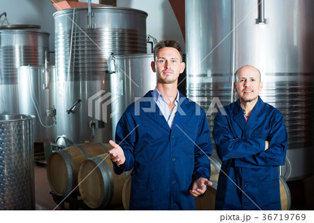 Two men in uniforms standing in winery fermentation compartment Two men in uniforms standing in winery fermentation compartment 36719769