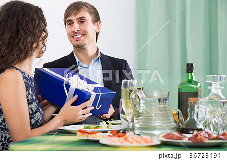 Woman presenting gift to man at table 36723494