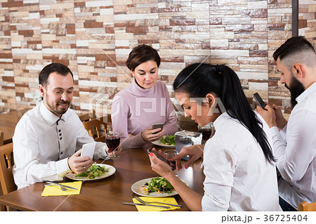 Smiling friends having dinner with smartphones 36725404