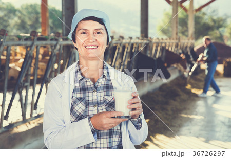 Female farmer is standing with glass of cow milk at the farm. Female farmer is standing with glass of cow milk at the farm. 36726297