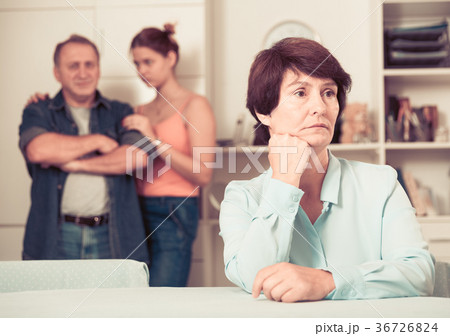 Upset mother is sitting at the table and her family is sympathying with her 36726824