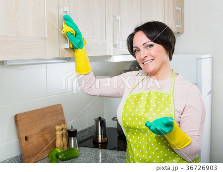 Middle aged woman dusting furniture in kitchen 36726903