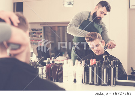 serious guy stylist creating haircut for man client at hairdressing salon serious guy stylist creating haircut for man client at hairdressing salon 36727265