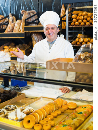 Senior smiling male staff offering fresh baguettes 36727398