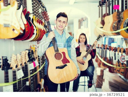 Teenagers examining guitars in shop 36729521