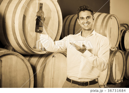 man holding bottle of wine in cellar with woods . 36731684