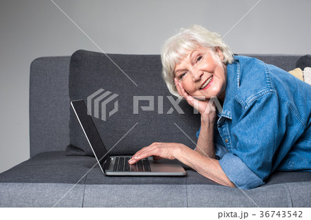 Old grey-haired lady relaxing on couch with gadget 36743542