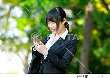 スマホを持ったスーツの女性　OL　ビジネス　スーツ　ポートレート　リクルート　緑背景　 36829436