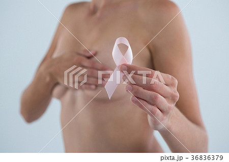Mid section of woman covering breast while showing pink ribbon Mid section of woman covering breast while showing pink ribbon 36836379