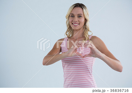 Portrait of smiling woman making heart shape on pink ribbon Portrait of smiling woman making heart shape on pink ribbon 36836716