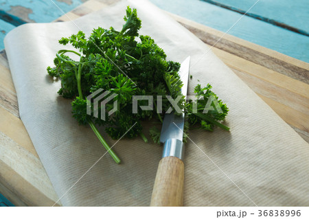 Coriander leaves, wax paper and knife on chopping board 36838996
