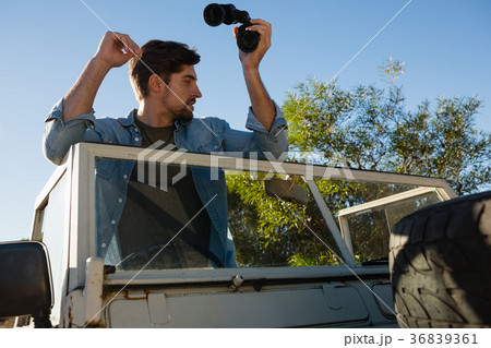 young man holding binoculars looking away while standing in off road vehicle 36839361
