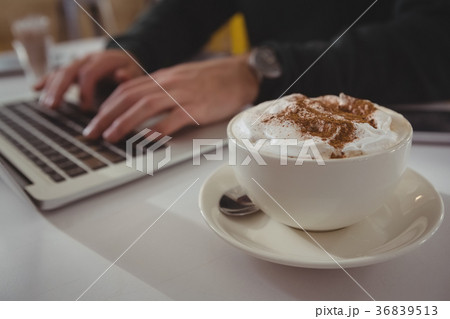 Cropped hands of businessman using laptop by coffee cup Cropped hands of businessman using laptop by coffee cup 36839513