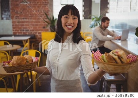 Portrait of waitress holding baskets with sandwiches while businessman using laptop 36839580