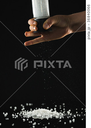 Mans hand sprinkling sea salt against black background 36840066