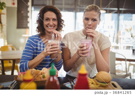 Portrait of smiling female friends drinking milkshake while sitting at cafe 36841265
