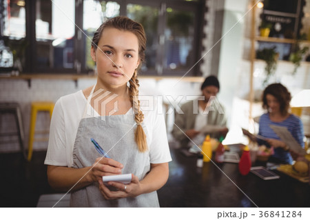 Confident young waitress standing with notepad at cafe Confident young waitress standing with notepad at cafe 36841284