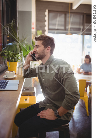 Smiling young man talking on cellphone while sitting at coffee shop Smiling young man talking on cellphone while sitting at coffee shop 36841395