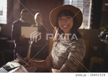 Portrait of smiling woman using smartphone against colleauges 36841529