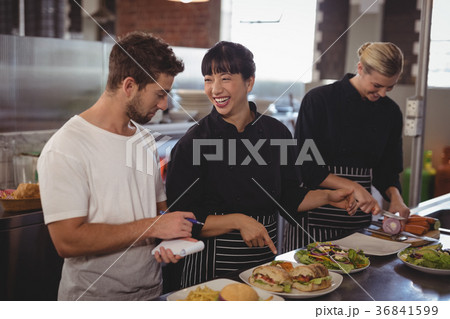 Cheerful chef pointing at food to waiter by female colleague Cheerful chef pointing at food to waiter by female colleague 36841599