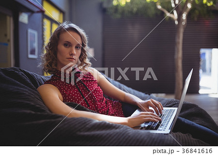 Portrait of confident young woman sitting with laptop on bean bag Portrait of confident young woman sitting with laptop on bean bag 36841616
