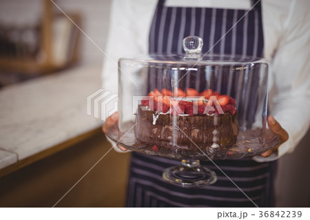 Midsection of waiter holding fresh cake on glass cakestand Midsection of waiter holding fresh cake on glass cakestand 36842239