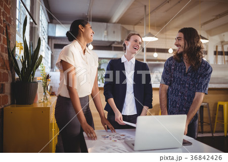 Cheerful young creative team standing by laptop on table Cheerful young creative team standing by laptop on table 36842426