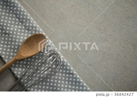 High anlge view of wooden spoon with wire whisk on folded napkin High anlge view of wooden spoon with wire whisk on folded napkin 36842427