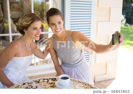 Bridesmaid taking selfie with bride in yard 36845802