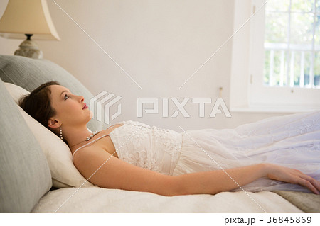 Thoughtful bride looking up while relaxing on bed 36845869