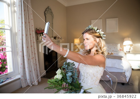 Happy bride taking selfie while sitting on chair in bedroom 36845922