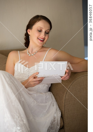 Happy bride reading wedding card while sitting on sofa Happy bride reading wedding card while sitting on sofa 36846057
