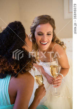 Bridesmaid whispering into bride ear while having champagne in bedroom Bridesmaid whispering into bride ear while having champagne in bedroom 36846079
