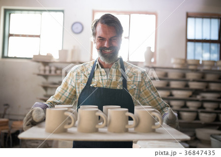 Happy male potter holding ceramic cups in tray Happy male potter holding ceramic cups in tray 36847435