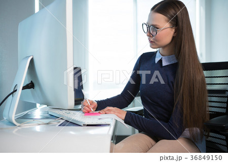 Female executive writing on sticky note at desk 36849150