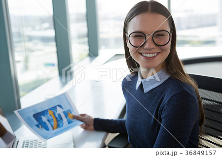 Portrait of female executive holding graph at desk 36849157