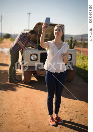Woman taking selfie with mobile phone while man repairing a car 36849386