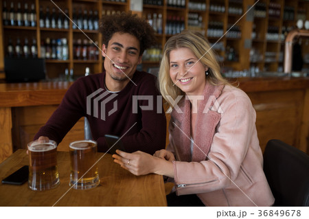 Smiling couple using mobile phone while having glass of beer in bar 36849678