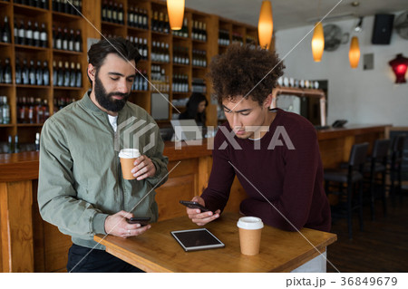 Two male friends using mobile phone while having coffee Two male friends using mobile phone while having coffee 36849679