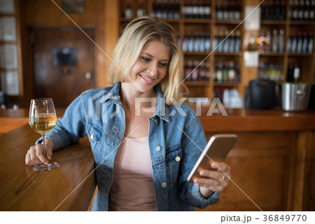 Smiling beautiful woman using mobile phone while having glass of wine Smiling beautiful woman using mobile phone while having glass of wine 36849770