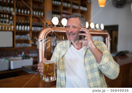 Smiling senior man talking on mobile phone while having glass of beer 36849936