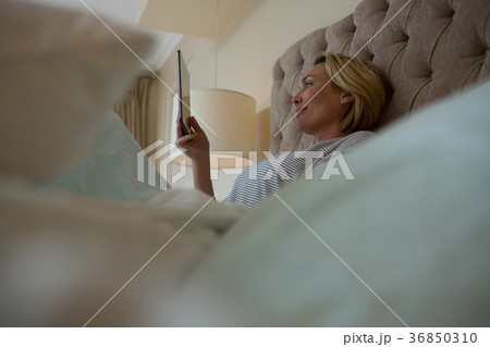 Woman using digital tablet while relaxing on bed 36850310